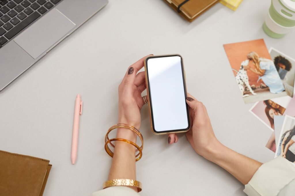 Hands holding a smartphone beside a notebook and coffee in daylight