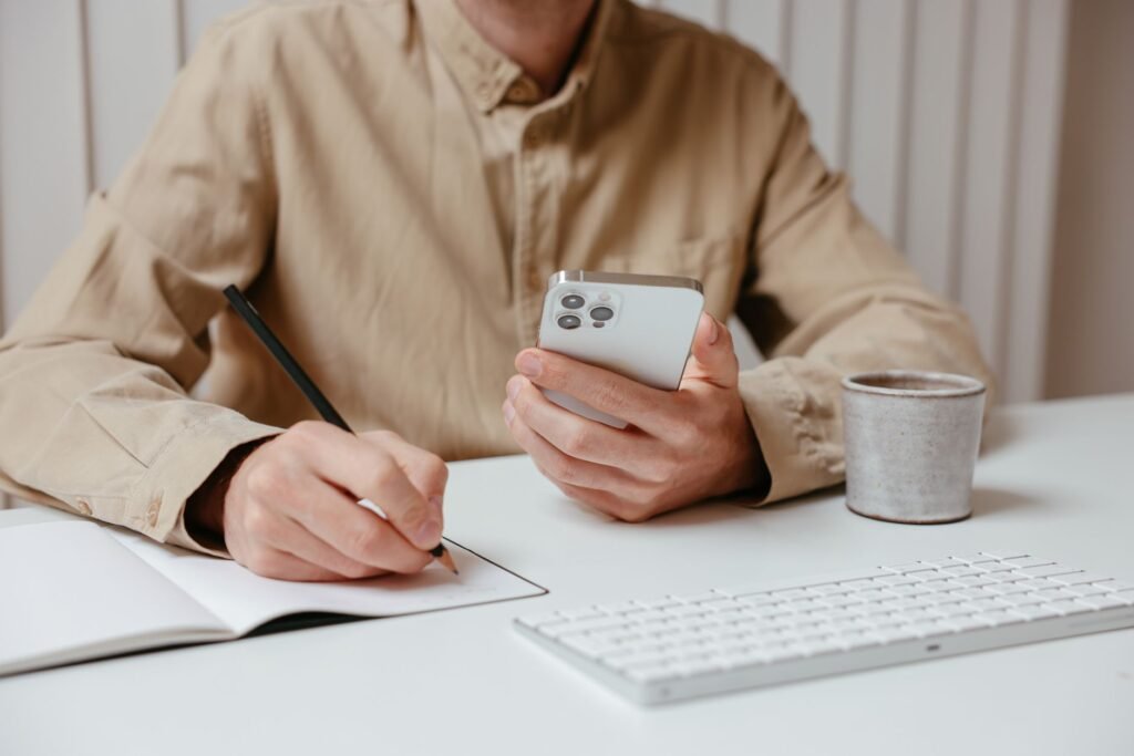 Hands holding a smartphone beside a notebook and coffee in natural daylight